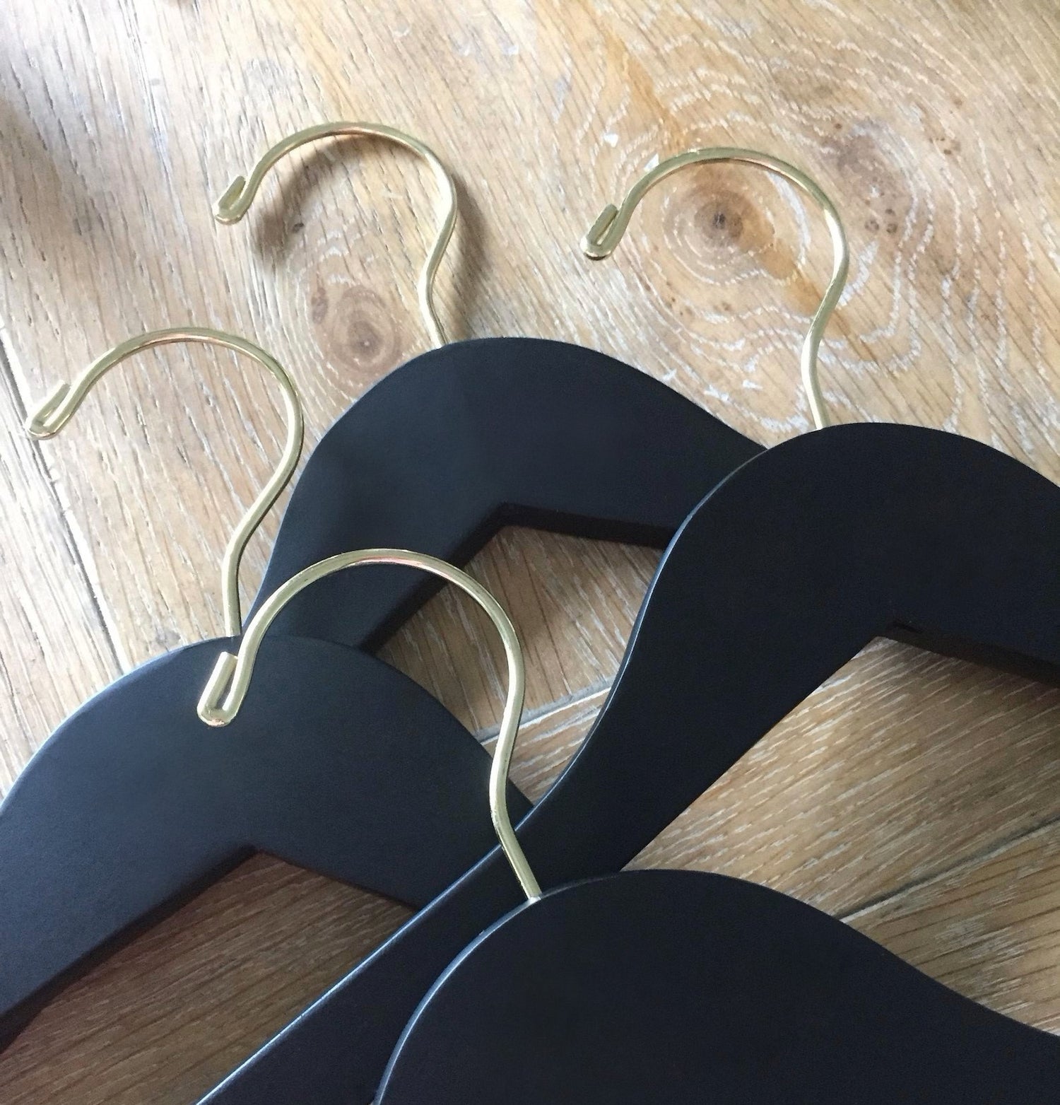 Four Matte Black Wood Adult Flat Suit Hangers with gold hooks for custom bridal hanger designers lying on wood floor