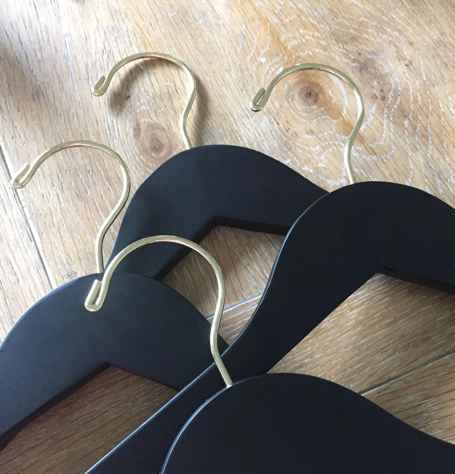 Four Matte Black Wood Adult Flat Suit Hangers with gold hooks for custom bridal hanger designers lying on wood floor