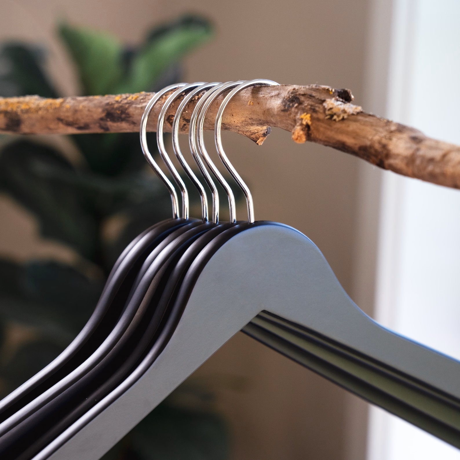 Matte Black Wooden Clothes Hangers with silver hooks hanging on a branch for home closets and retail spaces