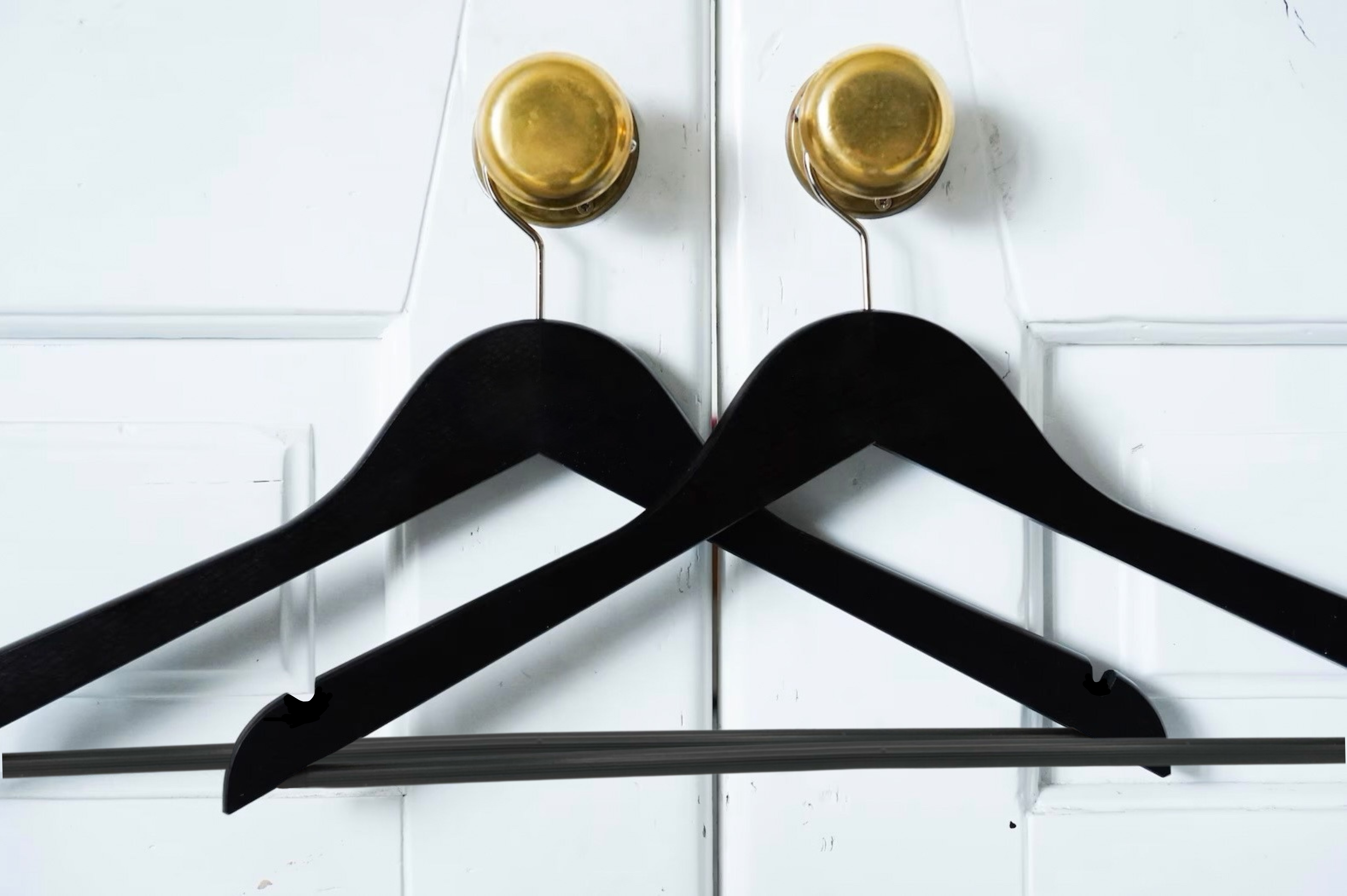 Two Matte Black Wooden Suit Hangers with pants bar for custom wedding hanger designers hanging on closet door’s doorknob