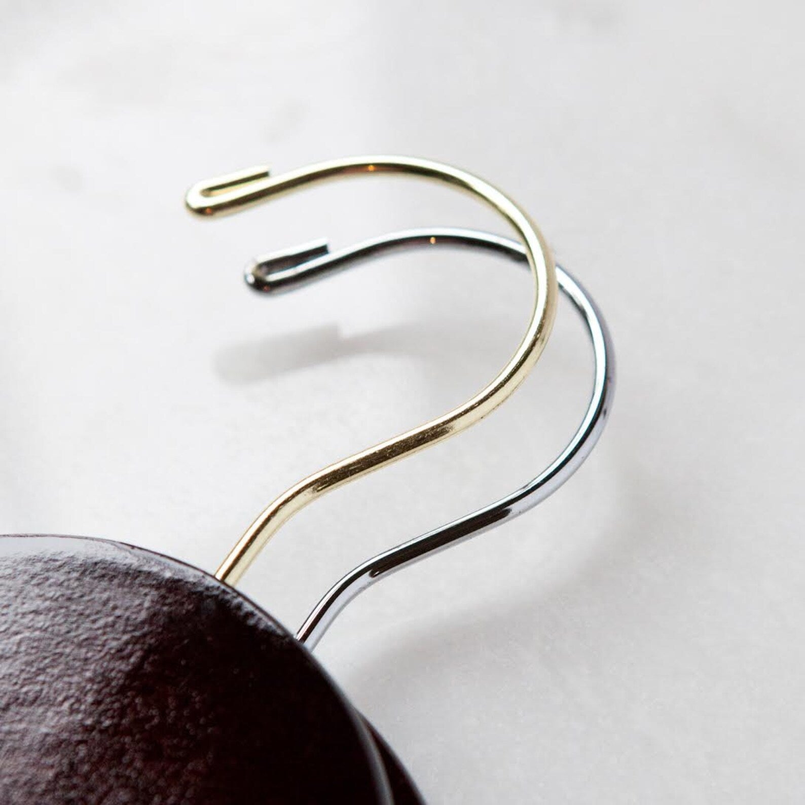The tops of a gold hooked dark walnut wood hanger stacked on top of a silver hooked dark walnut wood hanger