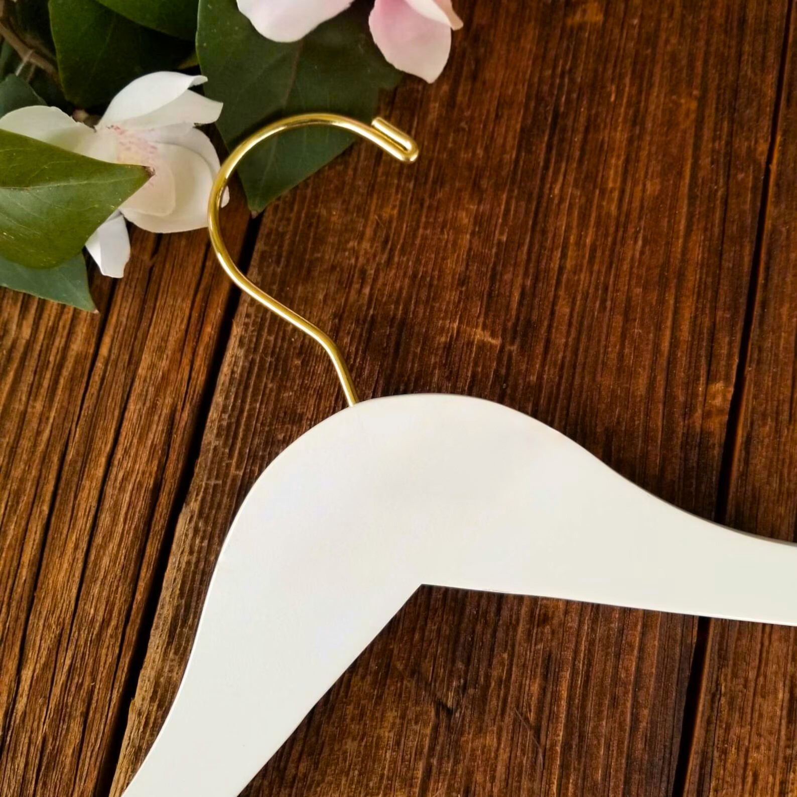 Luxury quality Ivory Wood Clothes Hanger with a gold hook lying on wooden table next to pink flowers