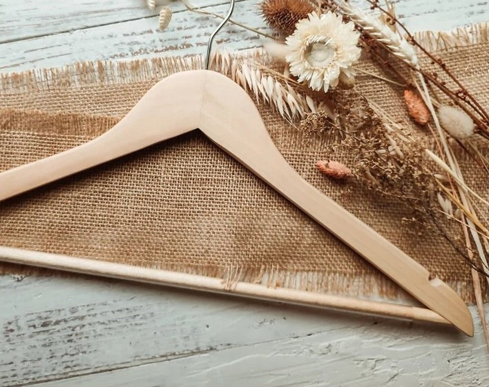Customizable Natural Wooden Adult Suit Hanger with non-slip pant bar lying on a table with cloth fabric and flowers