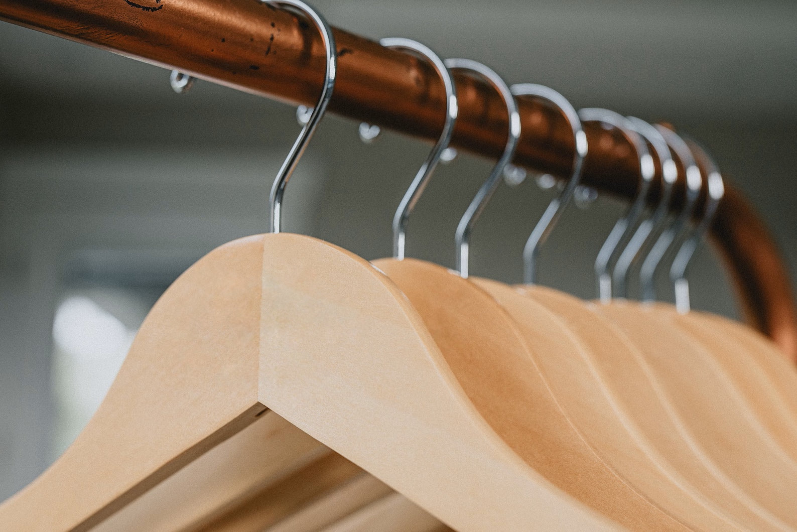 Customizable Natural No Notch Wooden Clothes Hangers with silver hooks hanging on a clothing rack