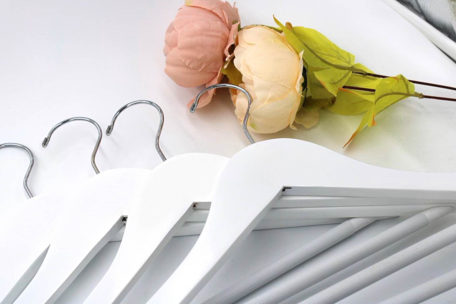 White Wood Flat Suit Hangers with silver hooks for residential closets and retail spaces lying on a table next to flowers