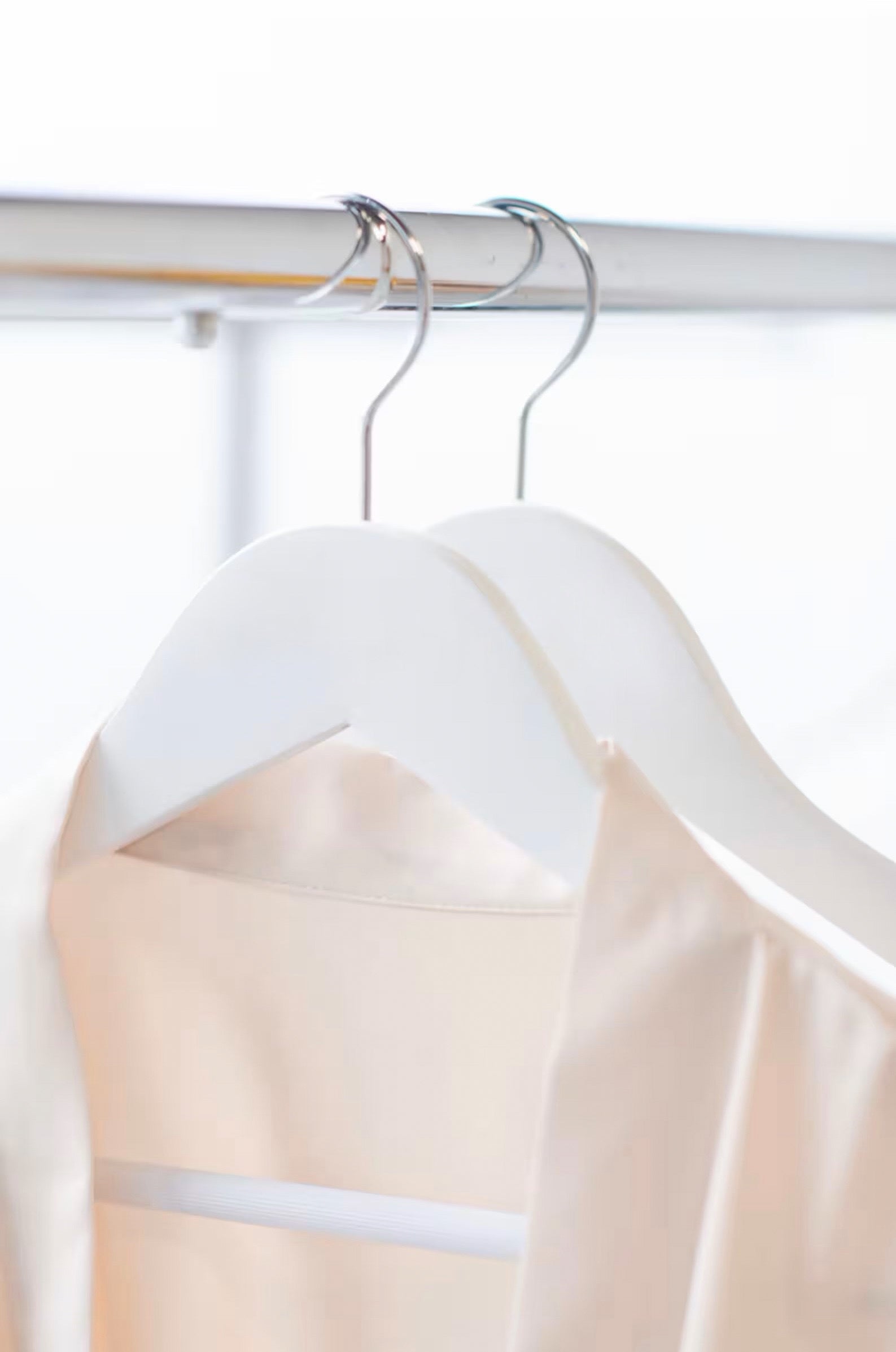 Wedding quality White Wood Suit Hangers with pant bar hanging on clothing rack with pink bridesmaid’s robes hanging on it