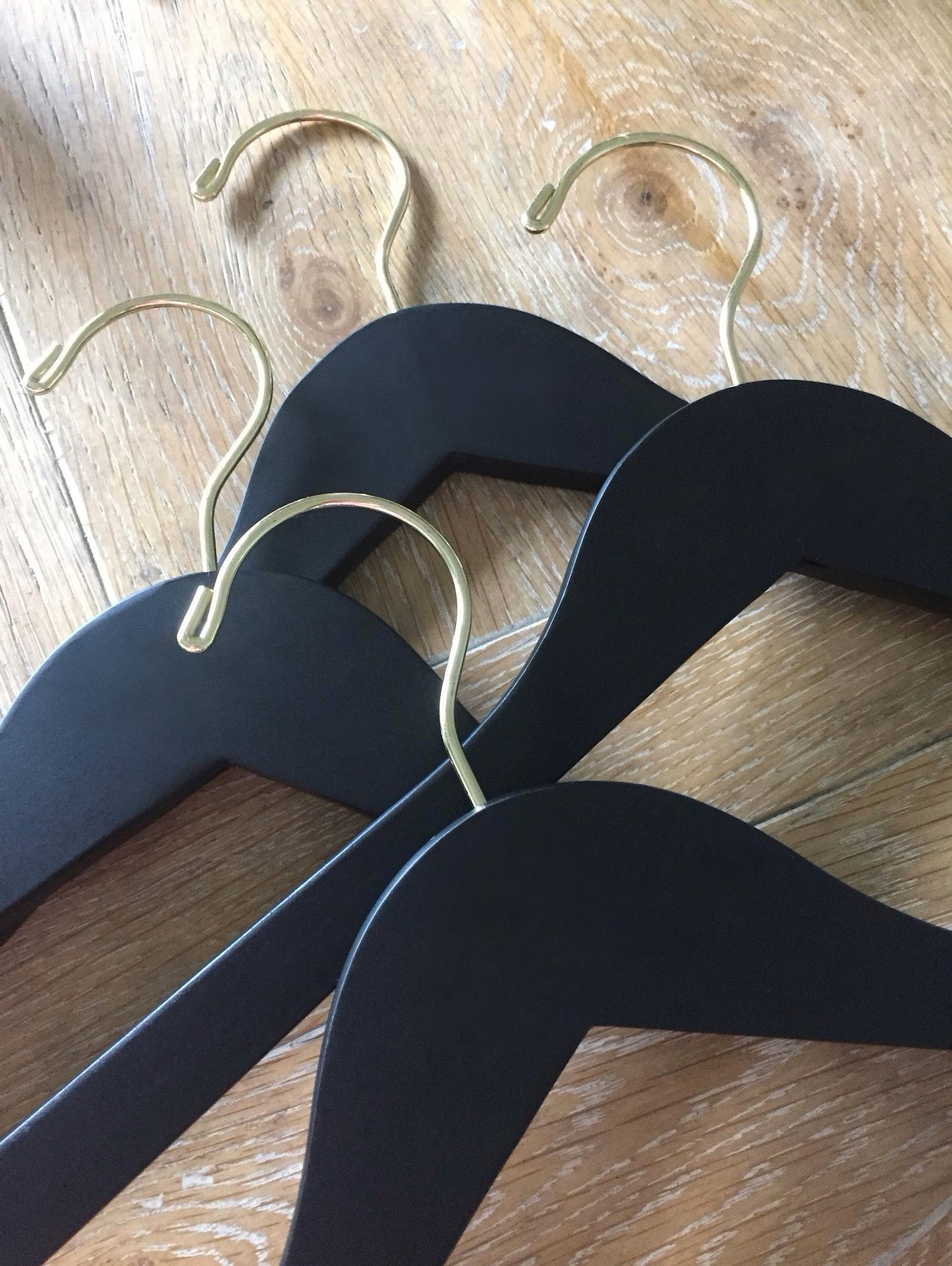 Four Matte Black Wood Adult Clothes Hangers with gold hooks for custom bridal hanger designers lying on wood floor 