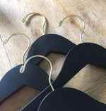 Load image into Gallery viewer, Four Matte Black Wood Adult Flat Suit Hangers with gold hooks for custom bridal hanger designers lying on wood floor #hook-color_gold-hook
