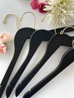 Load image into Gallery viewer, Four Matte Black Wooden Clothes Hangers with gold hooks for closets and stores lying on a table with flowers on it #hook-color_gold-hook
