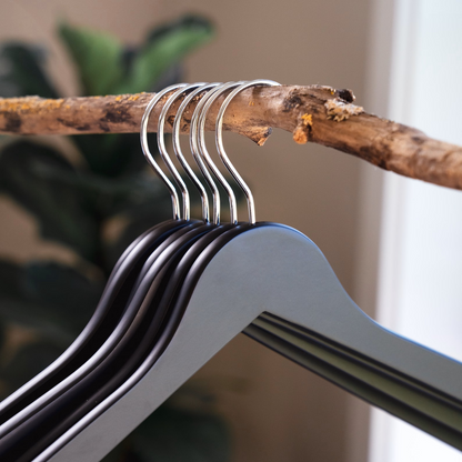 Matte Black Wooden Clothes Hangers with silver hooks hanging on a branch for home closets and retail spaces 