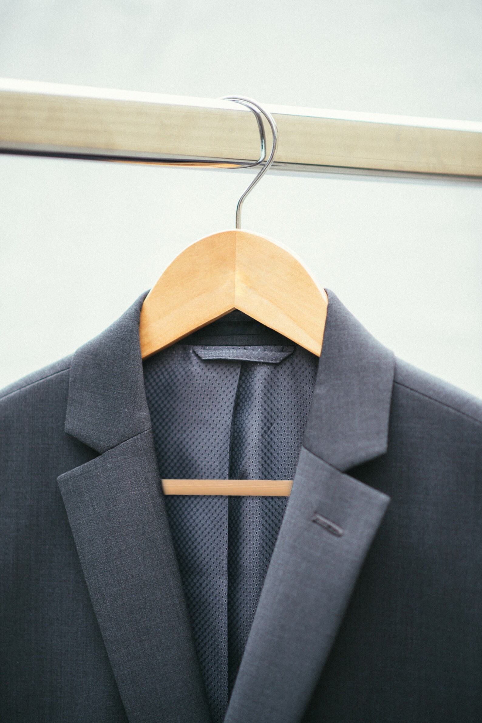 Natural Wooden Flat Suit Hanger for adults hanging on a rack with a men’s navy suit jacket hanging on it