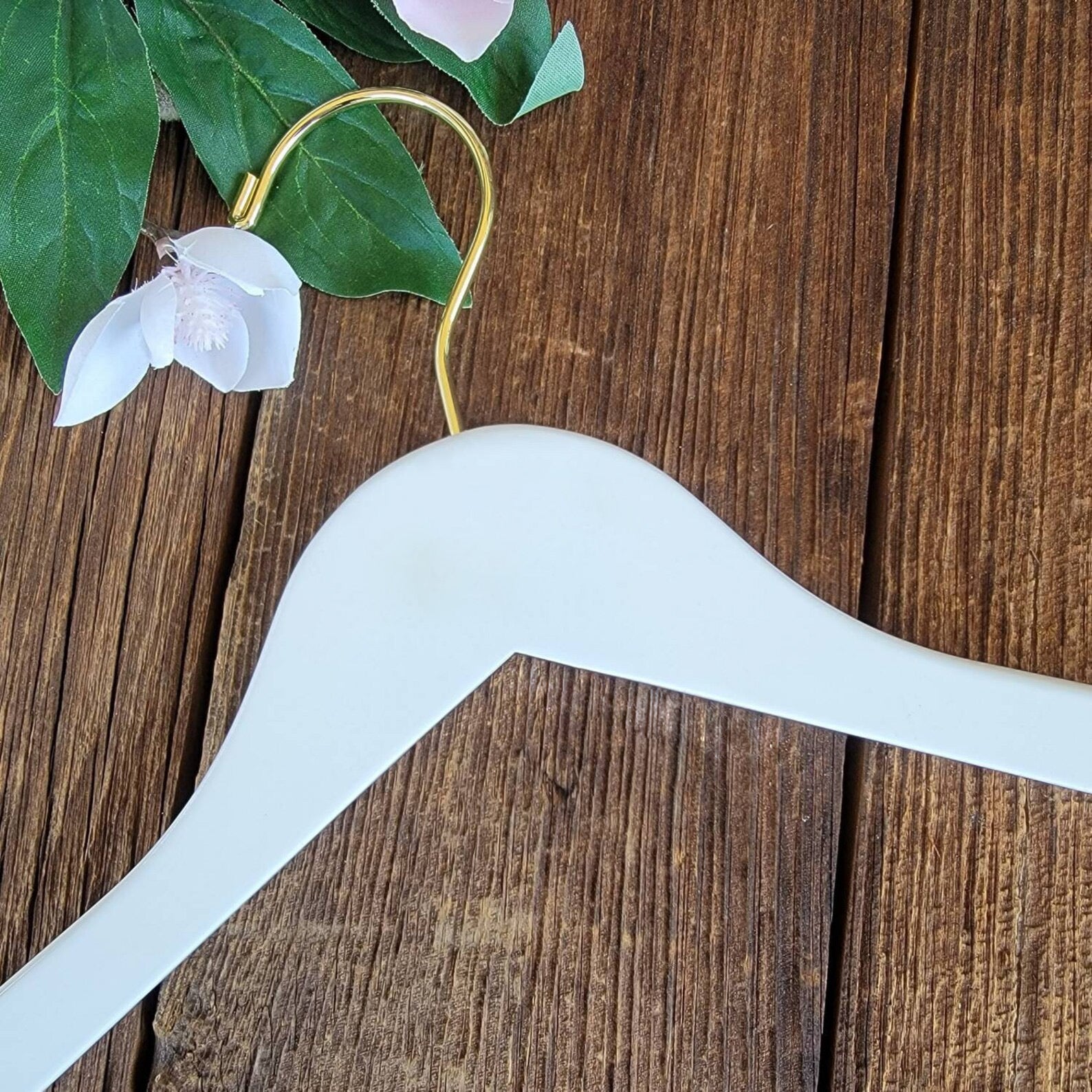 Luxury quality White Wood Flat Suit Hanger with a gold hook lying on wooden table next to white flowers #hook-color_gold-hook